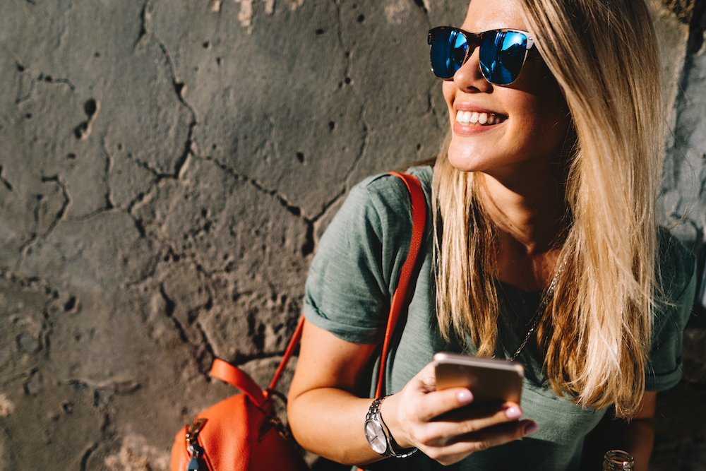 Portrait of a pretty smiling woman using mobile phone while holding drink