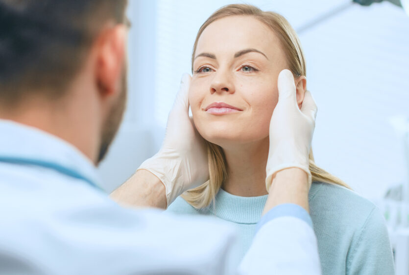 Doctor examining a woman’s face before Sculptra treatment, assessing skin and contours for facial rejuvenation and collagen restoration.