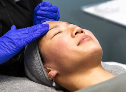 A client receiving a professional luxe facial as an aesthetic provider gently massages the forehead wearing blue gloves.