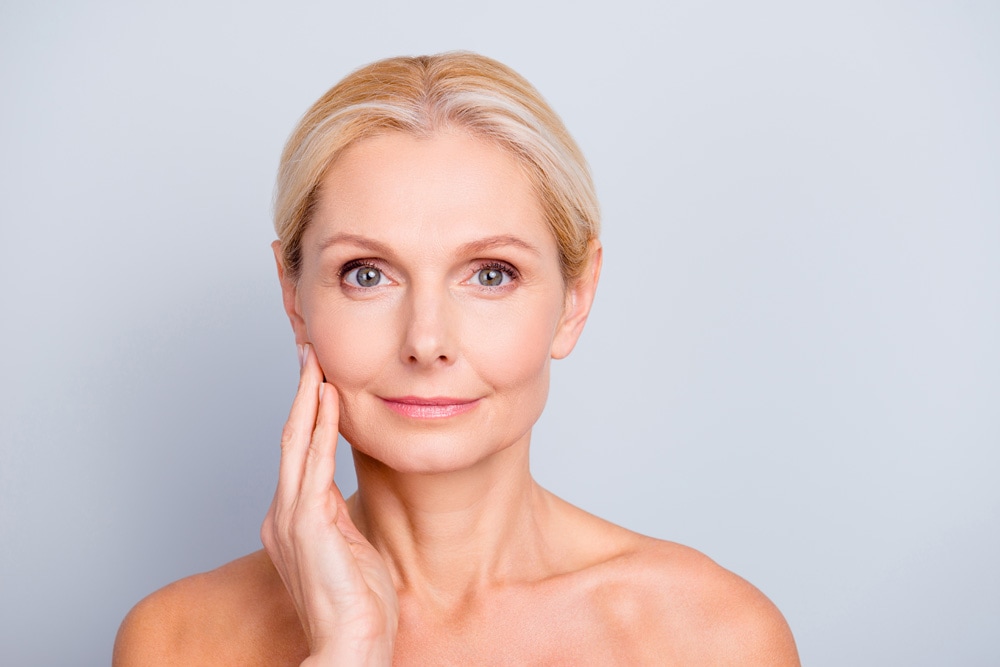 older white women touching her face with a gray background