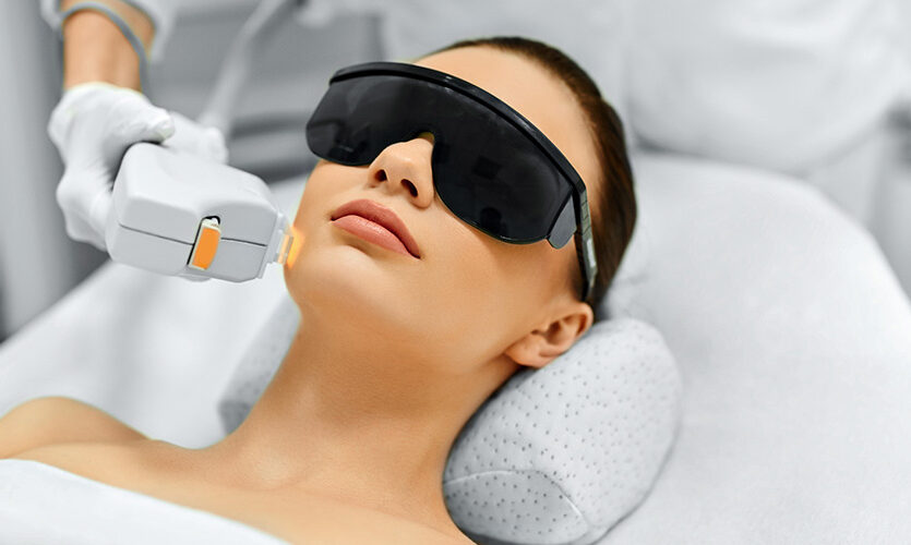 Woman receiving a facial laser or light-based skin treatment while wearing protective eye shields at a medical aesthetics clinic.
