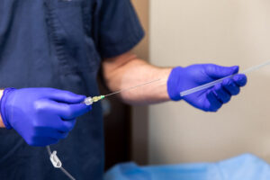 Doctor preparing an injection syringe while wearing blue medical gloves in a clinical setting.