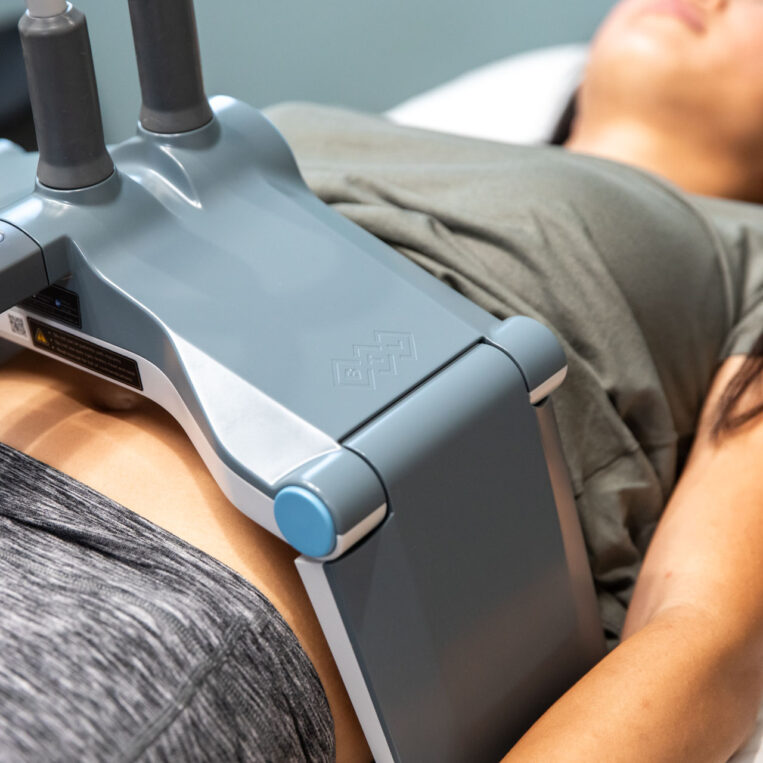 Woman undergoing a non-invasive body contouring treatment with an abdominal device at a medical aesthetics clinic.