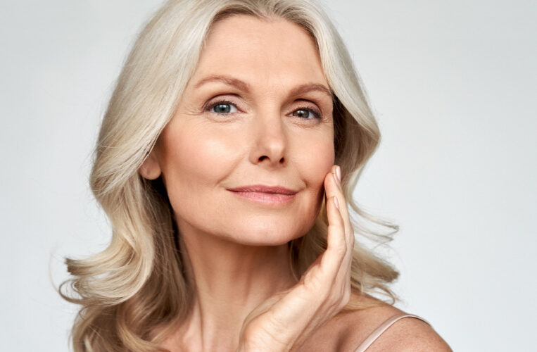 Confident mature woman with smooth, glowing skin touching her face, showcasing rejuvenated complexion after aesthetic treatment.