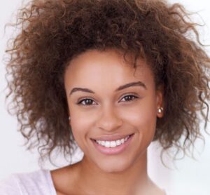 Smiling woman with natural curly hair and clear, healthy skin, representing radiant complexion and overall skin rejuvenation