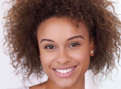 Smiling woman with natural curly hair and clear, healthy skin, representing radiant complexion and overall skin rejuvenation