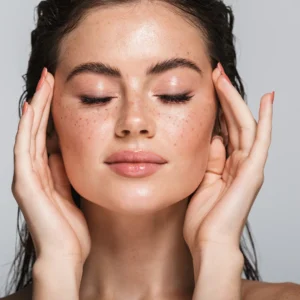 Close-up of a woman with eyes closed and hands gently touching her face, highlighting smooth skin, natural glow, and even skin texture