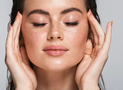 Close-up of a woman with eyes closed and hands gently touching her face, highlighting smooth skin, natural glow, and even skin texture