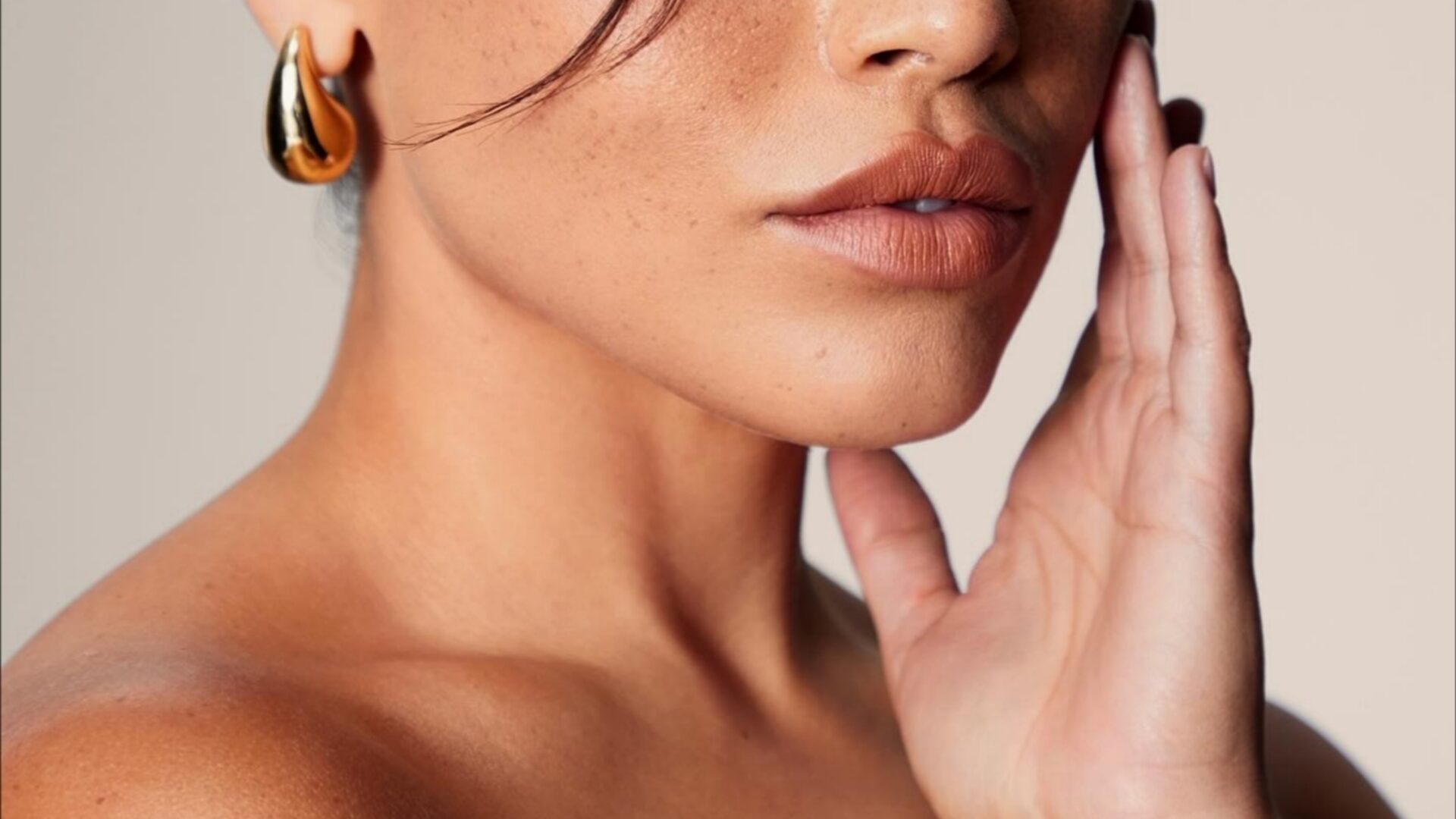 A woman touches the side of her face, showing smooth skin and a defined jawline.